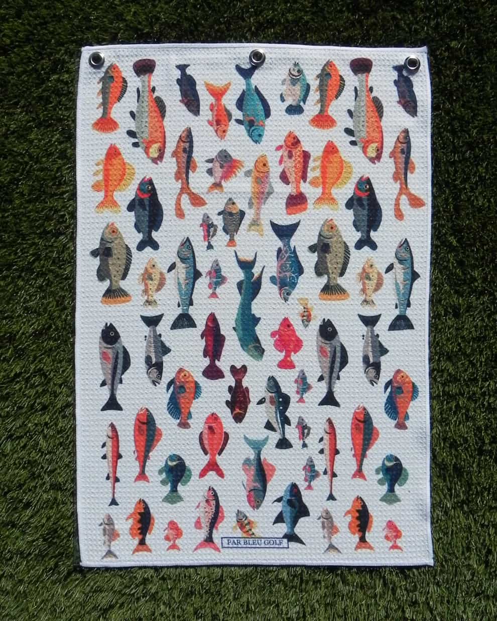 Colorful Fishies microfiber golf towel laid flat on green grass, showcasing full pattern and size.