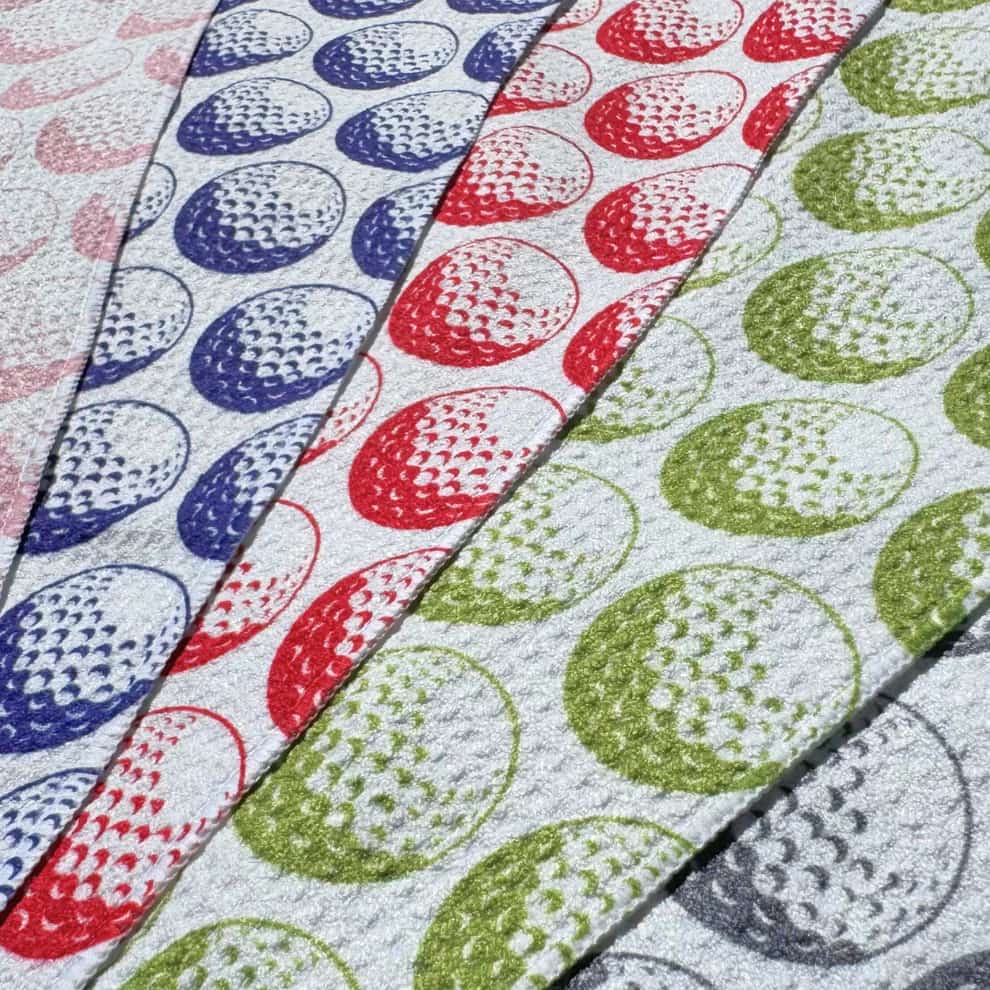 Close-up of five golf ball towels in blue, red, pink, gray, and green, stacked diagonally—great for gifting or mixing and matching.