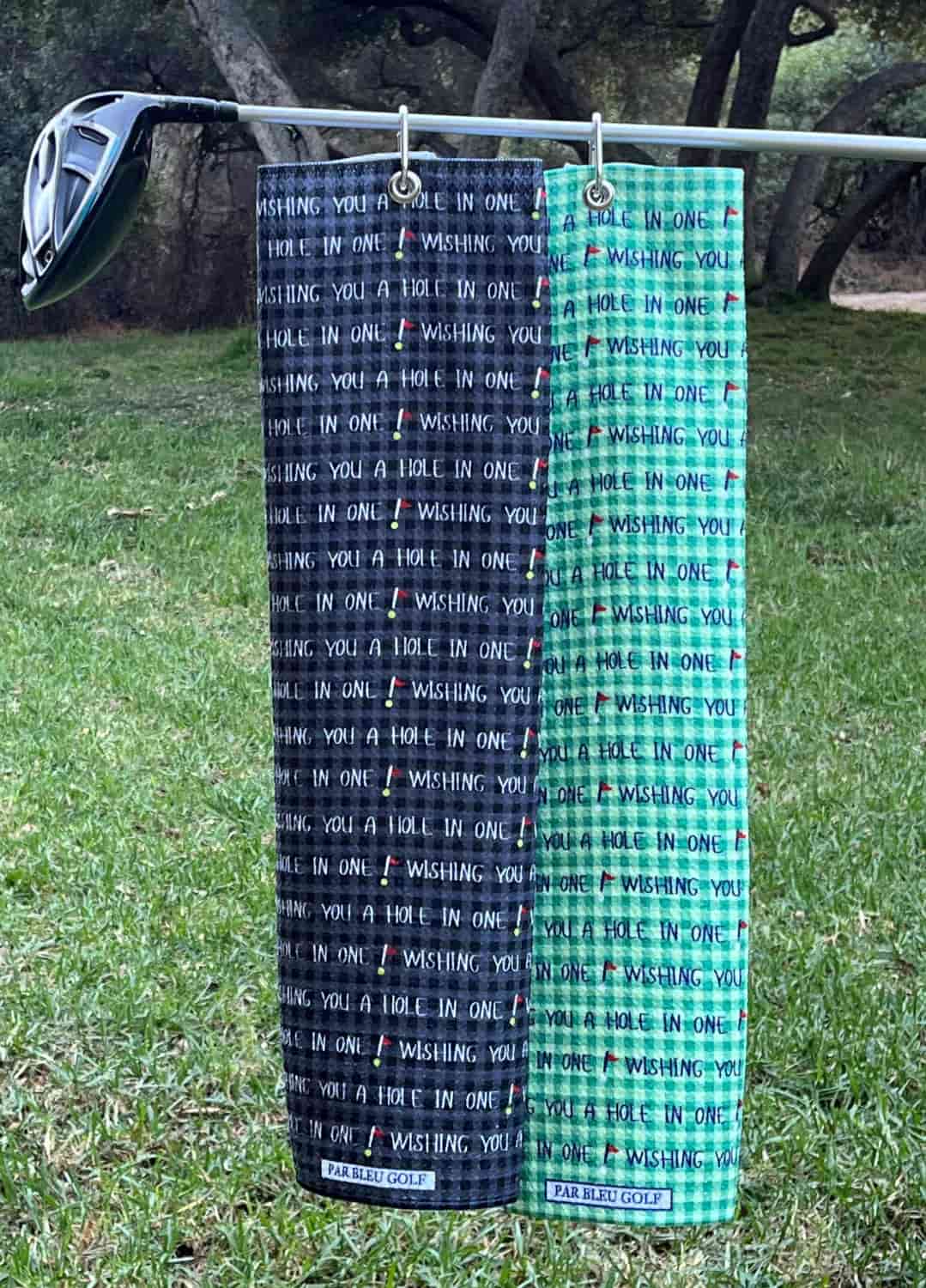 Green and black Hole in One towels displayed together outdoors, perfect pair for golf gifts or matching sets