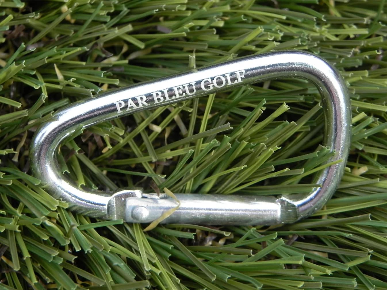 Silver carabiner on grass, included with each towel for easy attachment to your golf bag or cart.
