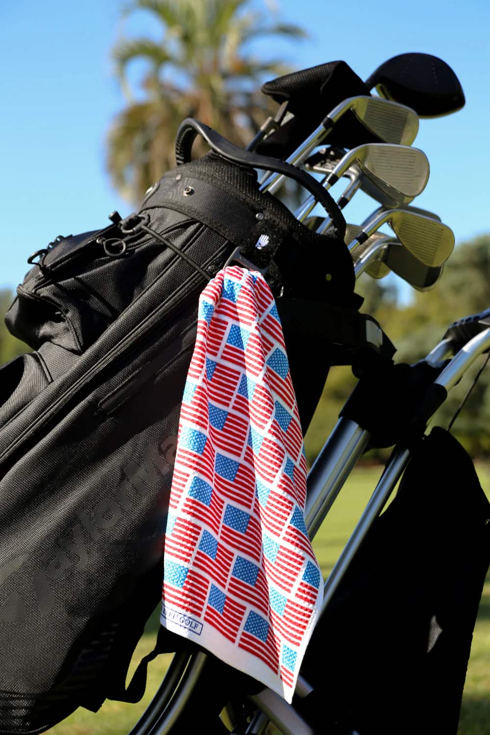 Patriotic golf towel hanging on a black golf bag with clubs, blending utility and Americana style.