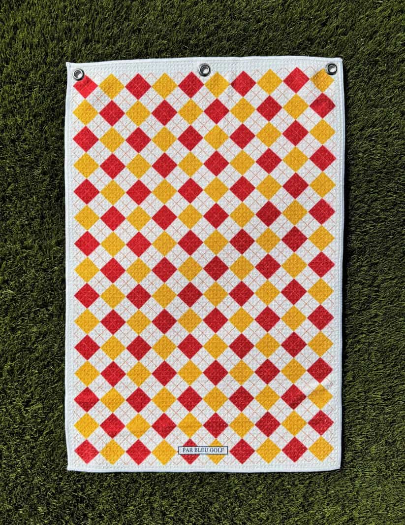 The Argyle Chipper: Cardinal & Gold microfiber golf towel laid flat on grass showing full plaid design