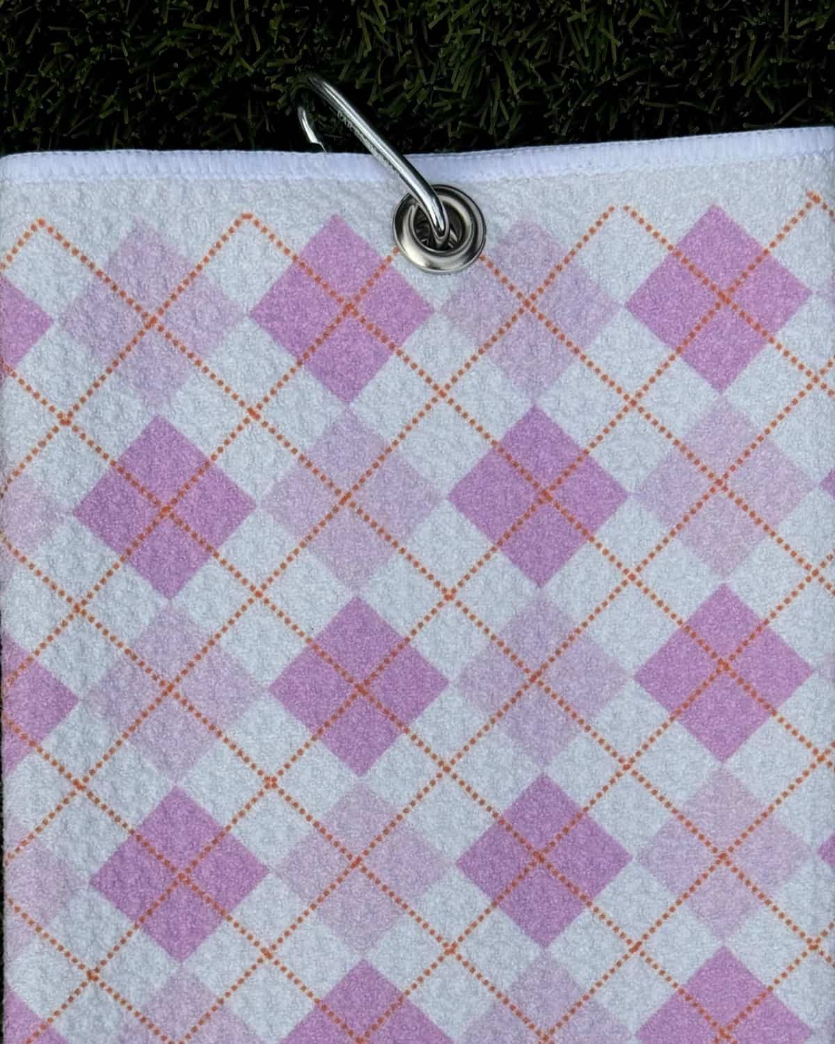 Pink plaid microfiber golf towel with argyle pattern hanging by durable carabiner clip
