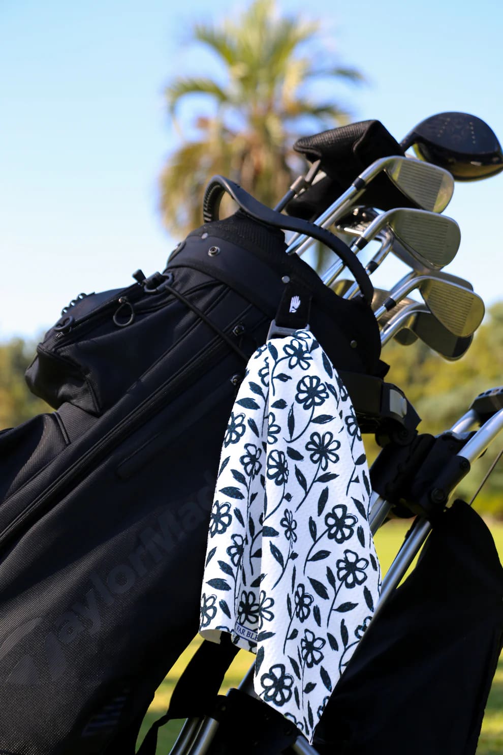 The Black Daisy towel clipped to golf bag on sunny course, perfect stylish golf gift