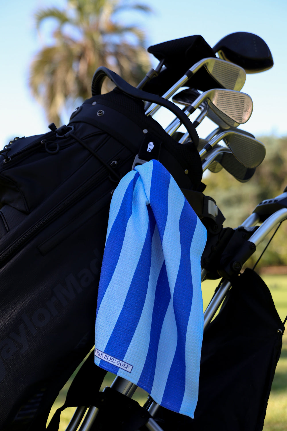 Blue and navy striped golf towel clipped to golf bag on a sunny course