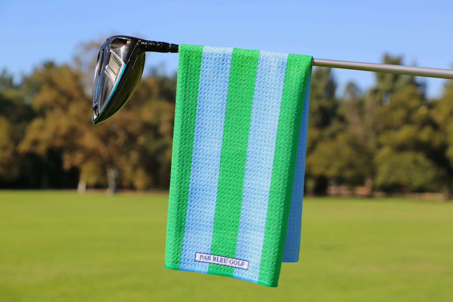 Blue and green striped golf towel hanging on a club with lush fairway in the background