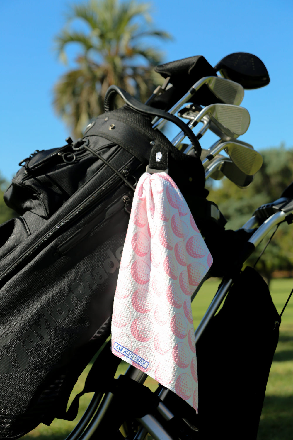 Pink golf towel clipped to golf bag on a sunny day with palm trees