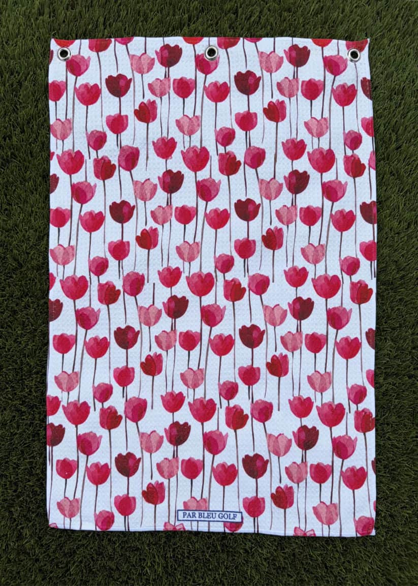 Red tulip golf towel laid flat on green grass, showcasing feminine floral design and soft microfiber material