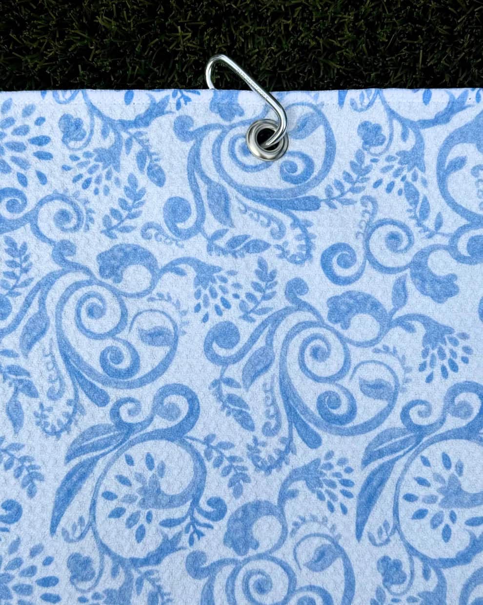 The Toile: Blue golf towel with floral toile design hanging vertically from carabiner