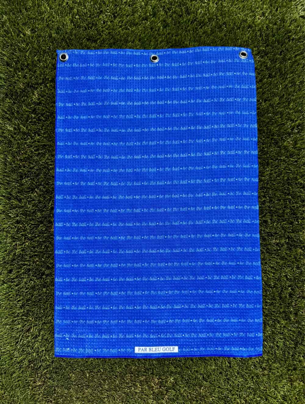 Be The Ball golf towel displayed on the course with grass in the background – bold lettering and premium microfiber construction shown in outdoor setting