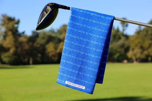 Be The Ball golf towel folded over a golf club – microfiber towel with bold white lettering displayed on the course