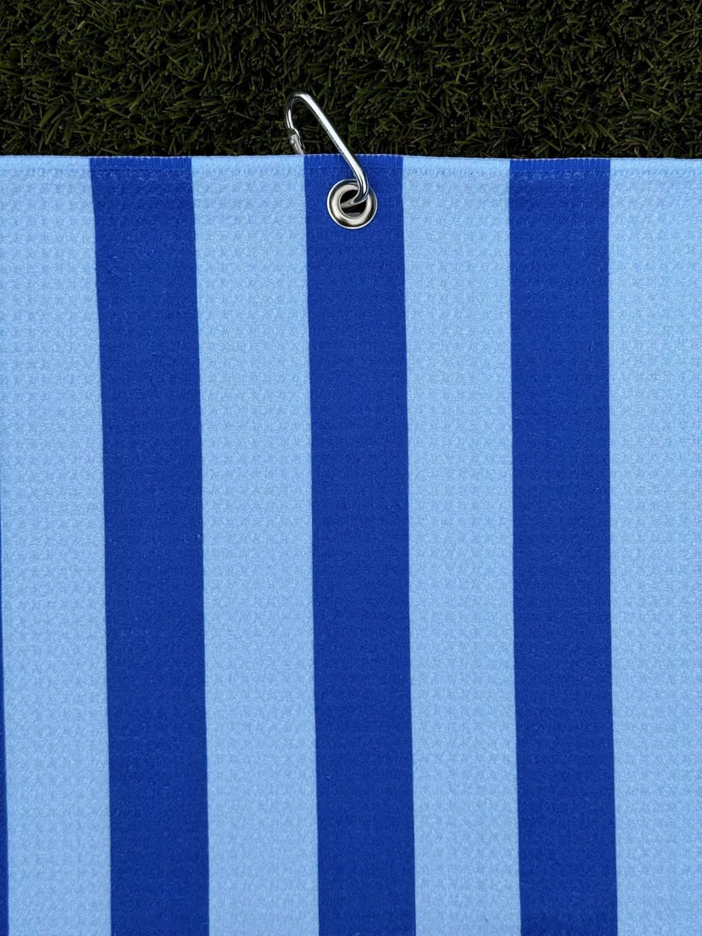 Blue and navy striped golf towel hanging vertically with metal carabiner clip