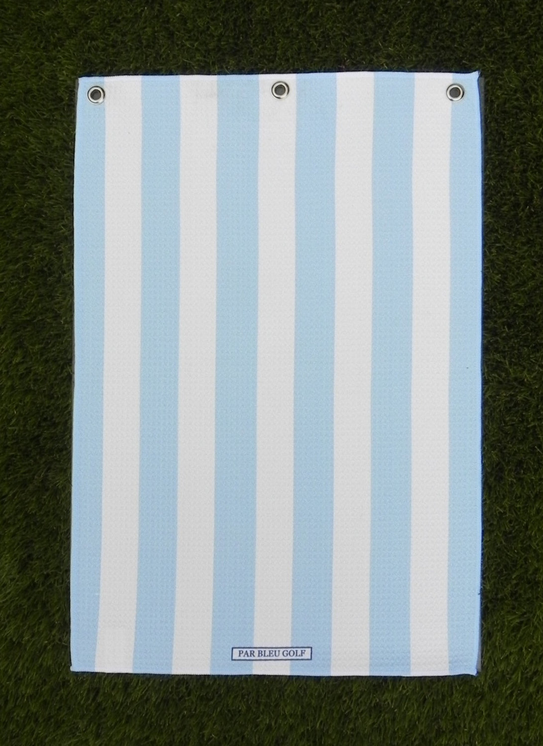 Cabana Stripe golf towel in blue and white laid flat on grass, showing clean stripe pattern