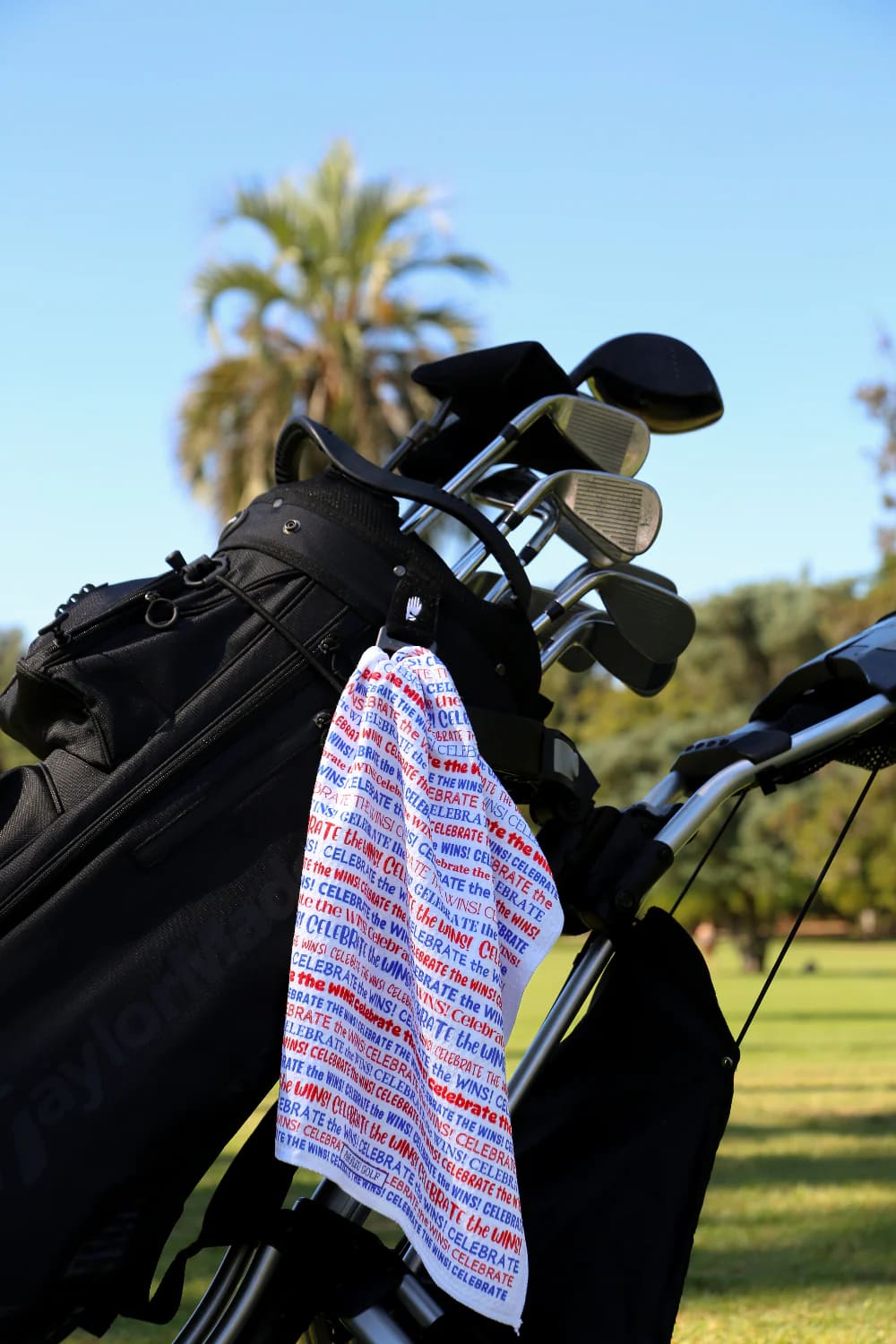 Celebrate the Wins golf towel clipped to a golf bag, ideal for on-course motivation and easy cleaning