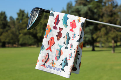 Colorful Fishies golf towel hanging on a golf club with vibrant koi fish print and green course background