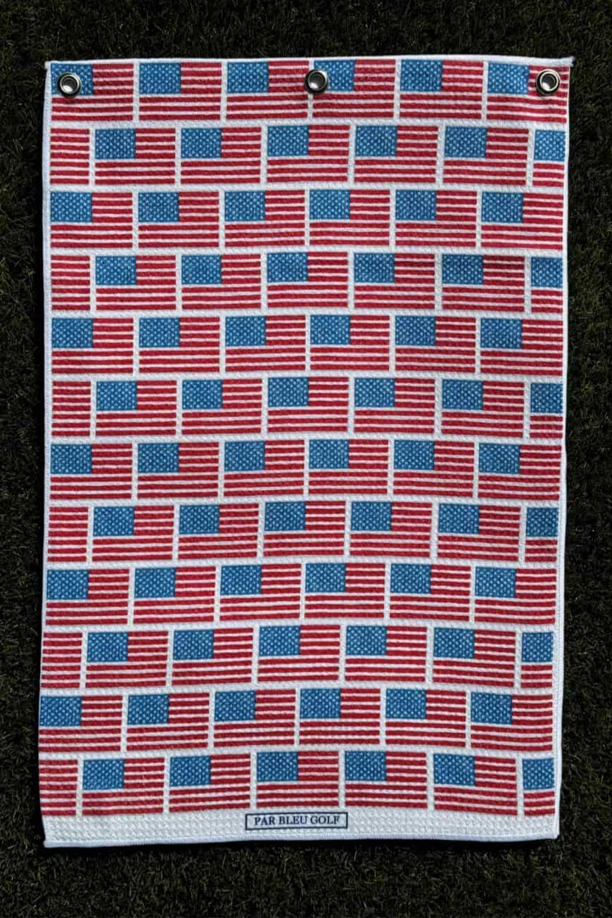 Golf towel with American flag design laid out on turf for full product visualization and sizing reference.