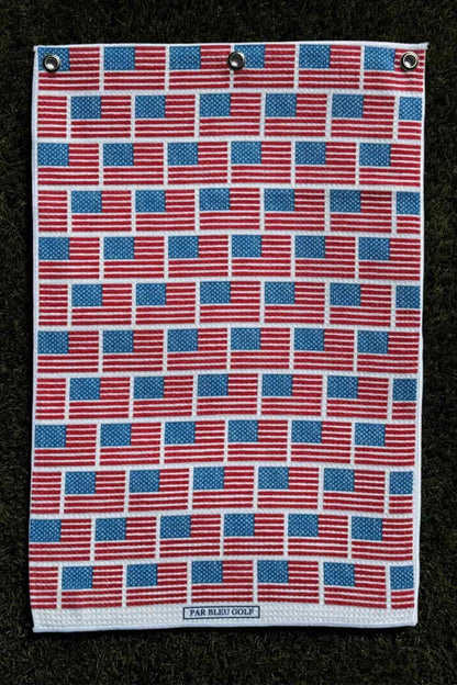 Golf towel with American flag design laid out on turf for full product visualization and sizing reference.