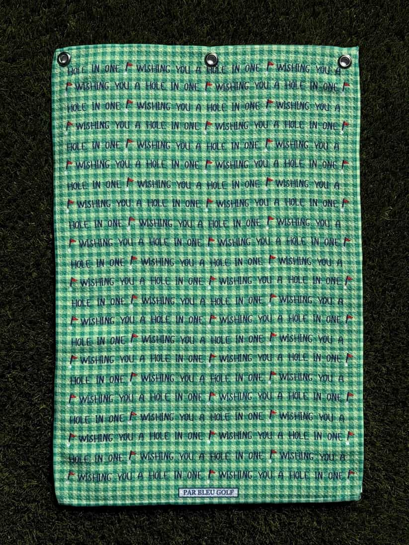 Golf towel with motivational message shown laid flat on grass, soft green microfiber material