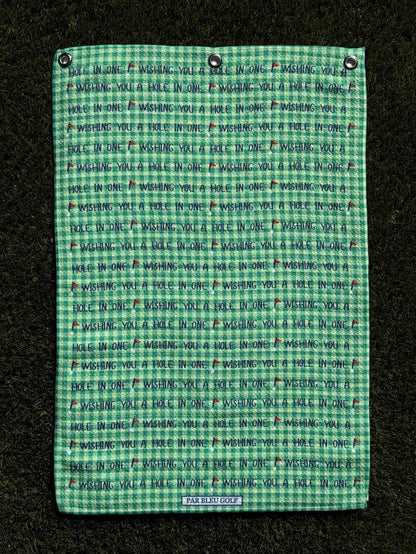 Golf towel with motivational message shown laid flat on grass, soft green microfiber material