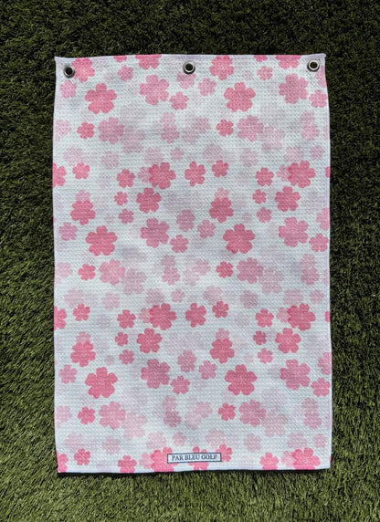 Pretty in Pink Floral women’s golf towel laid flat on green grass, showcasing cherry blossom print and premium fabric