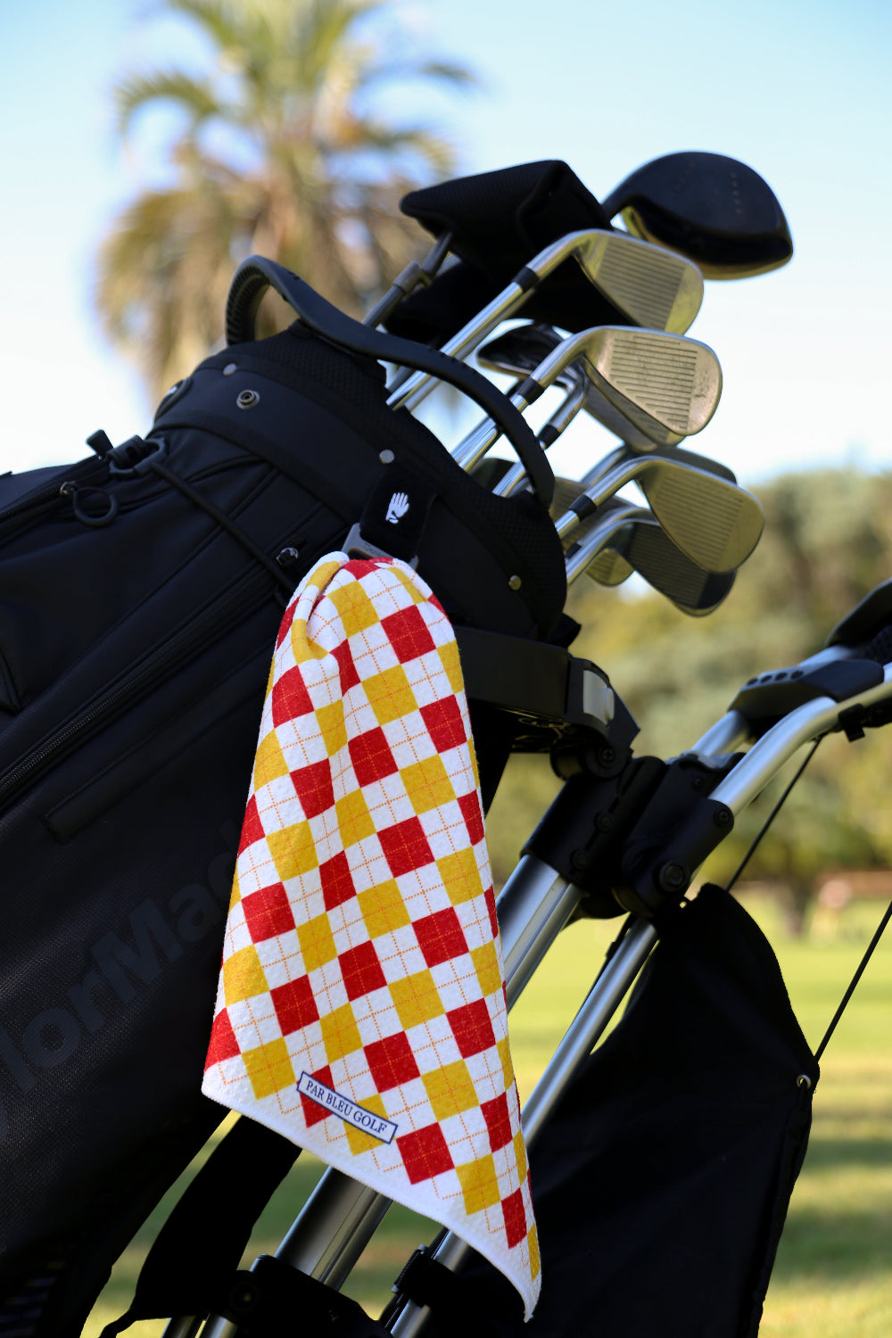 Red and yellow plaid golf towel clipped to golf bag with palm trees in background