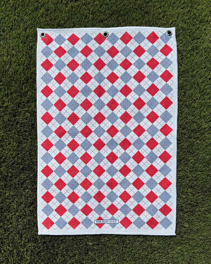 Red and grey plaid golf towel laid flat on grass, featuring soft microfiber and stylish diamond design