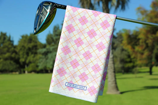Pink argyle golf towel hanging on a club with palm trees and green fairway in background