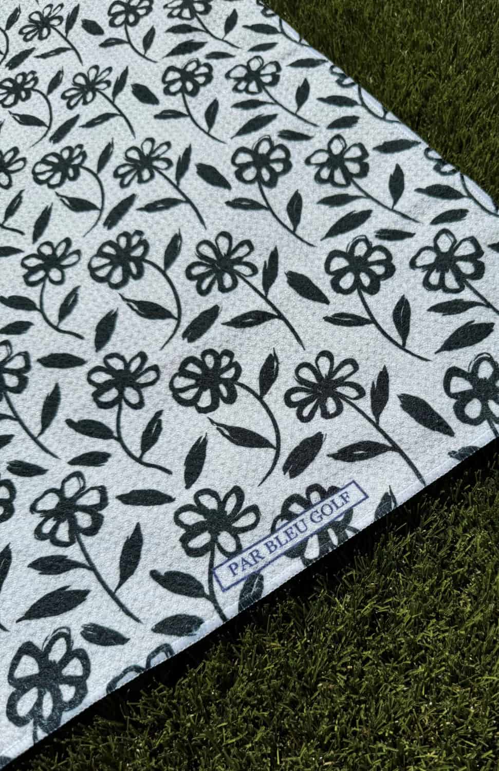 Close-up of The Black Daisy microfiber golf towel featuring black daisy pattern and Par Bleu logo