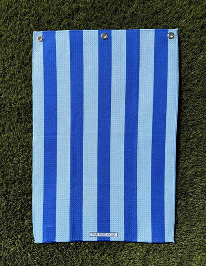 Blue & navy Cabana Stripe towel laid flat on green grass showing full design
