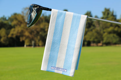 Blue and white striped golf towel hanging on club with trees and clear sky in background
