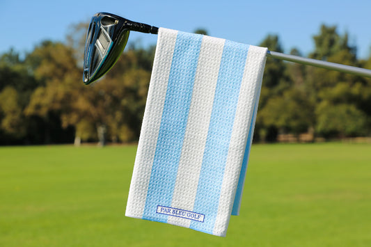 Blue and white striped golf towel hanging on club with trees and clear sky in background