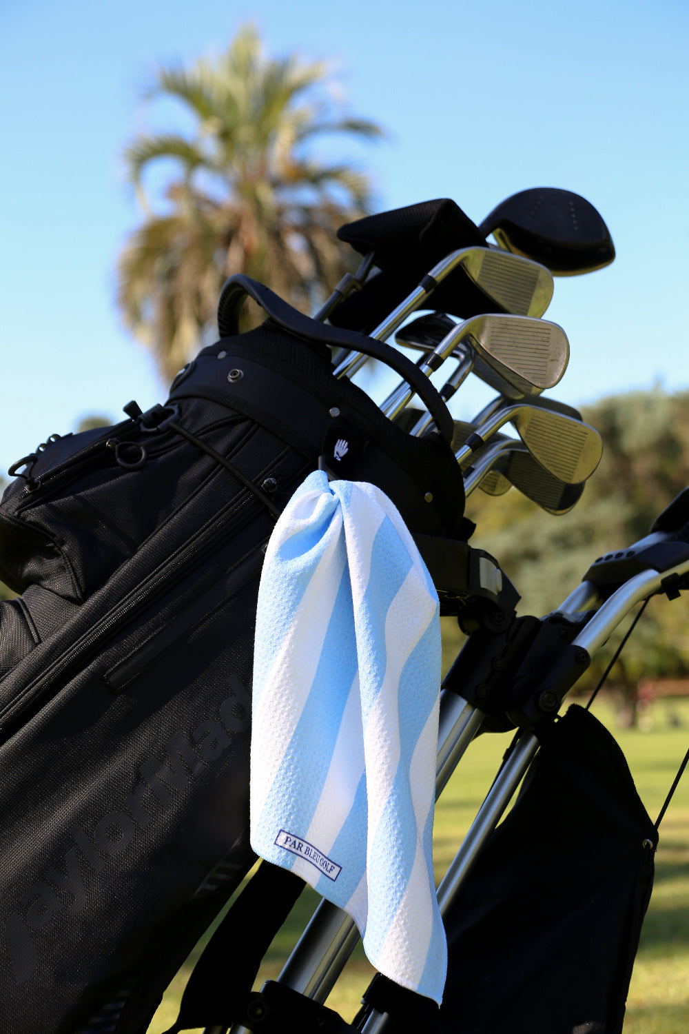 Blue and white striped golf towel clipped to a golf bag on a sunny course