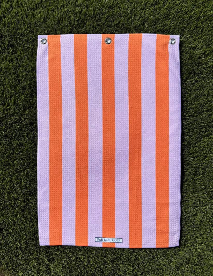 Pink and orange striped golf towel laid flat on grass, showing soft microfiber texture