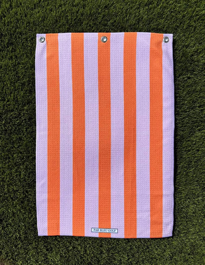 Pink and orange striped golf towel laid flat on grass, showing soft microfiber texture