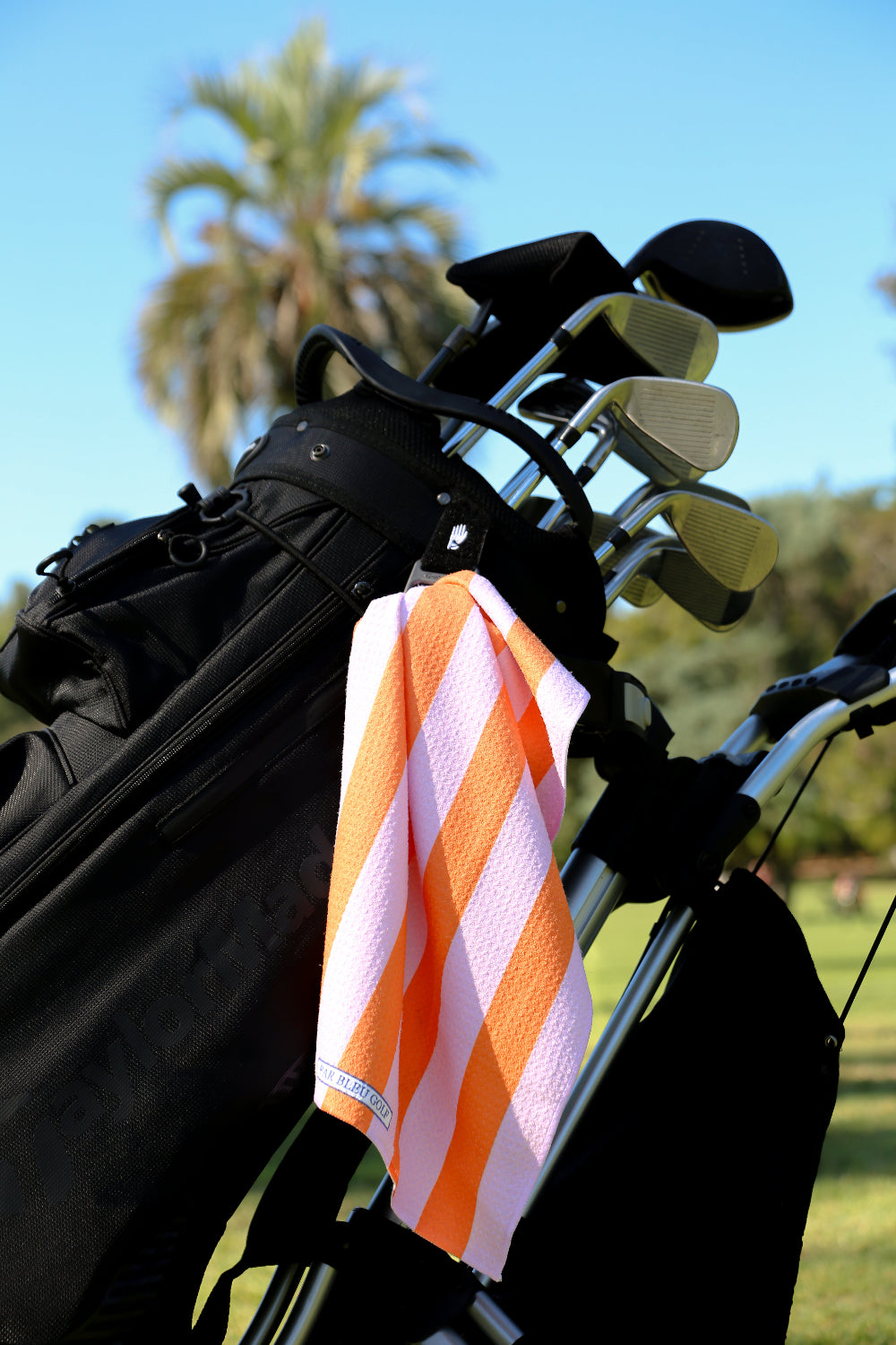 Vibrant striped golf towel clipped to black golf bag with palm trees in background