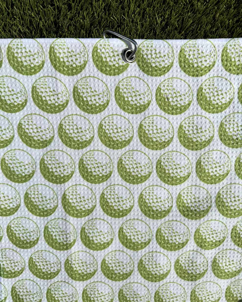 Green golf towel with golf ball print hanging by carabiner clip