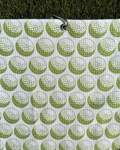 Green golf towel with golf ball print hanging by carabiner clip