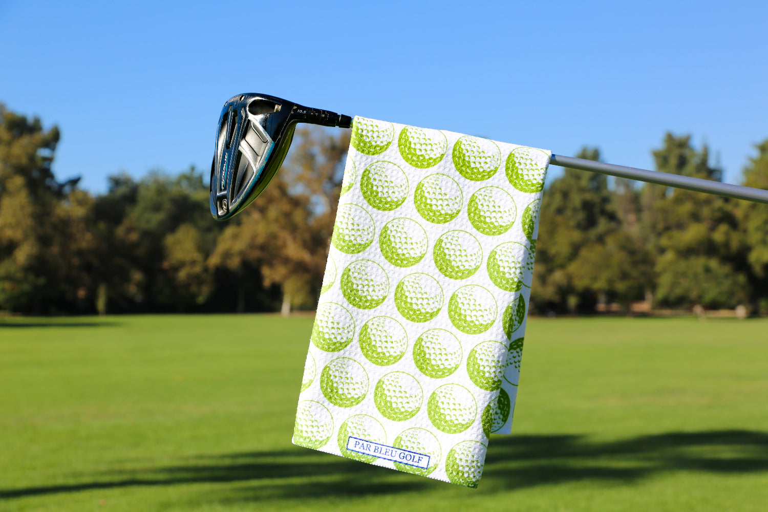 Green golf towel hanging on a club over a bright fairway with blue sky