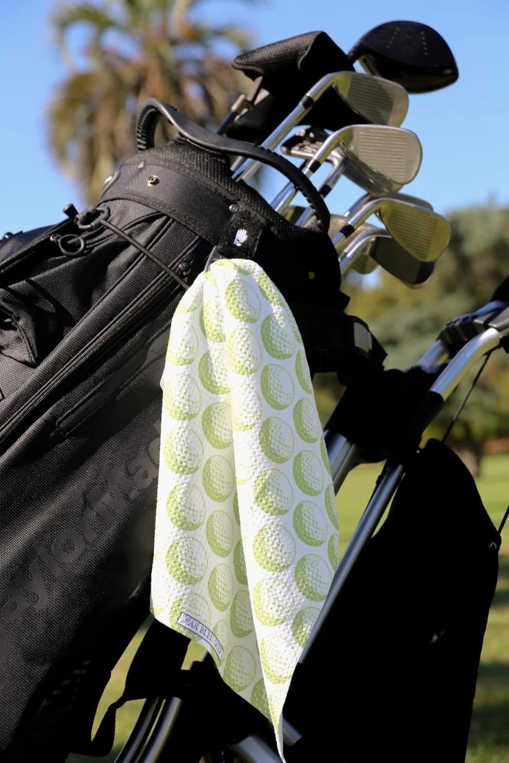 Green golf towel clipped to golf bag with trees and sky in background