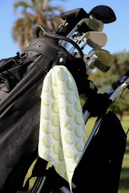Green golf towel clipped to golf bag with trees and sky in background