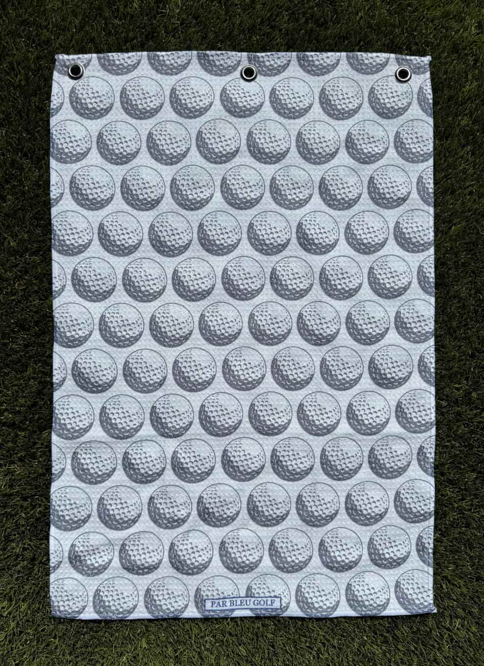 The Golf Ball: Grey microfiber towel laid flat on grass showing golf ball print design