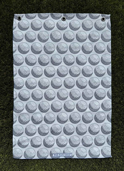 The Golf Ball: Grey microfiber towel laid flat on grass showing golf ball print design