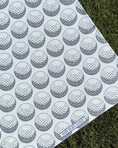 Close-up of The Golf Ball: Grey towel showing Par Bleu Golf logo and golf ball texture