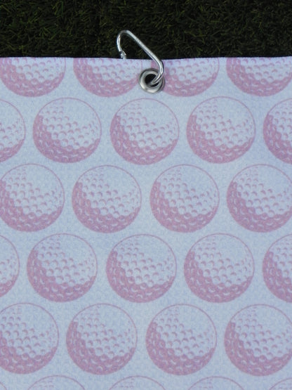 Pink golf towel hanging by metal carabiner, showing repeating golf ball print