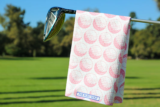 Pink golf towel hanging on a club over a green fairway with trees and blue sky