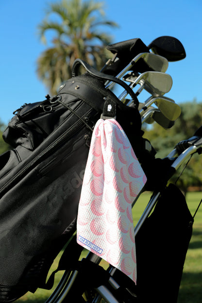 Pink golf towel clipped to golf bag on a sunny day with palm trees