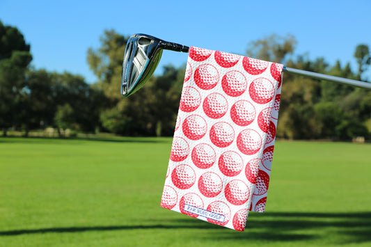 Red golf towel hanging on a club with green fairway and blue sky in the background