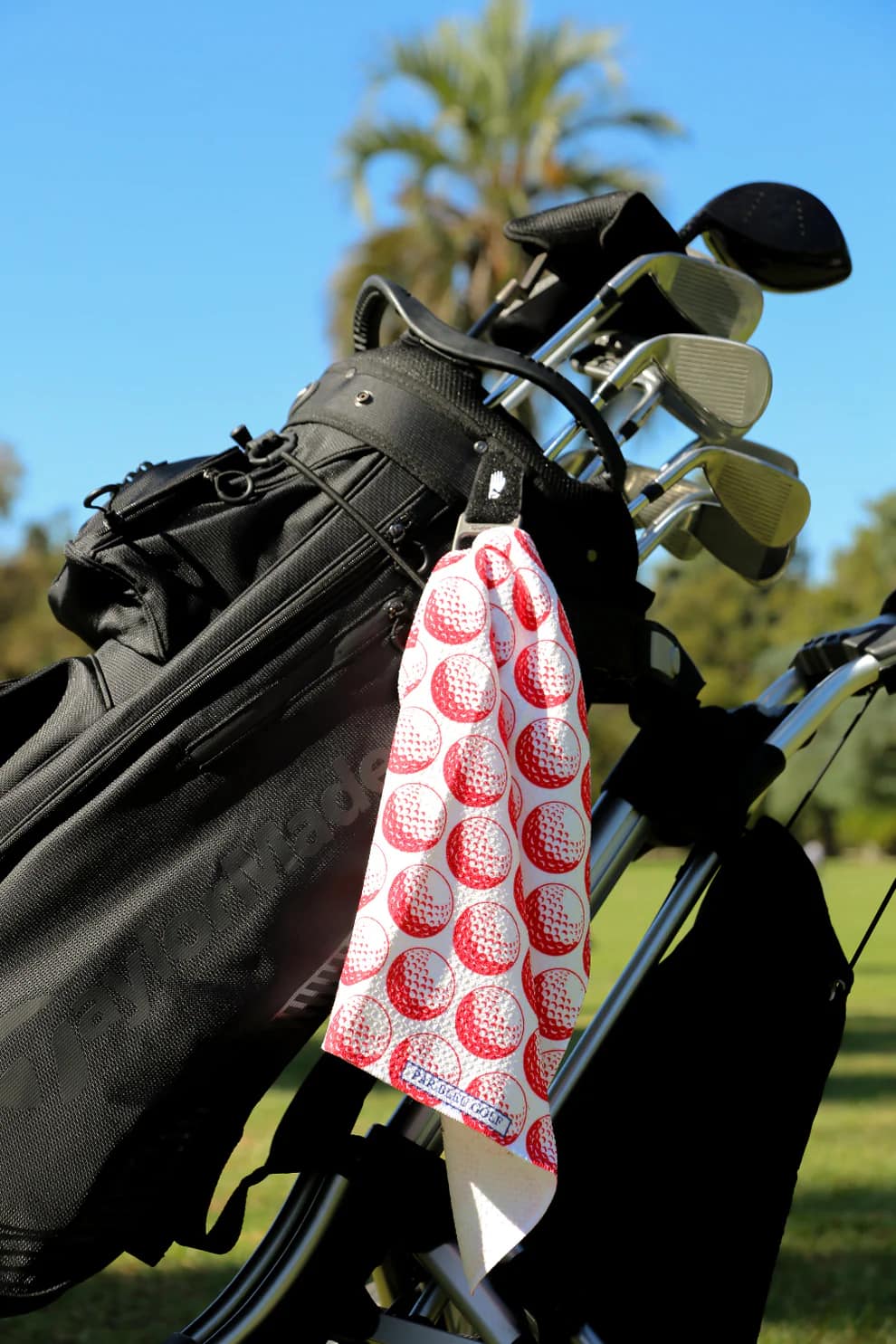 Red golf towel clipped to a golf bag with palm trees and blue sky