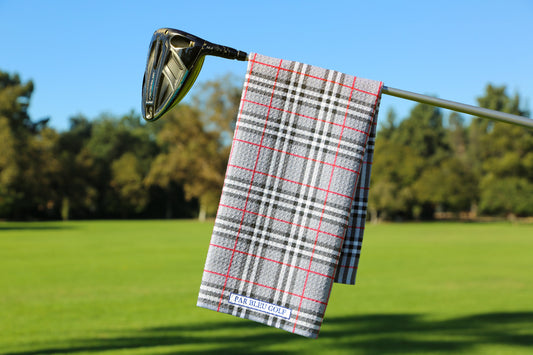 Grey plaid golf towel hanging on a club over a green fairway with trees in the background