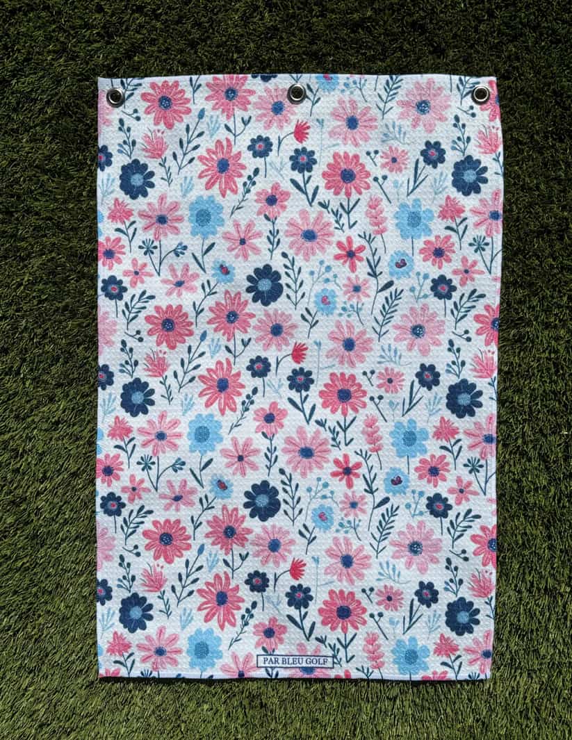 The Pink & Navy Floral golf towel laid flat on grass showing charming pattern and soft microfiber fabric